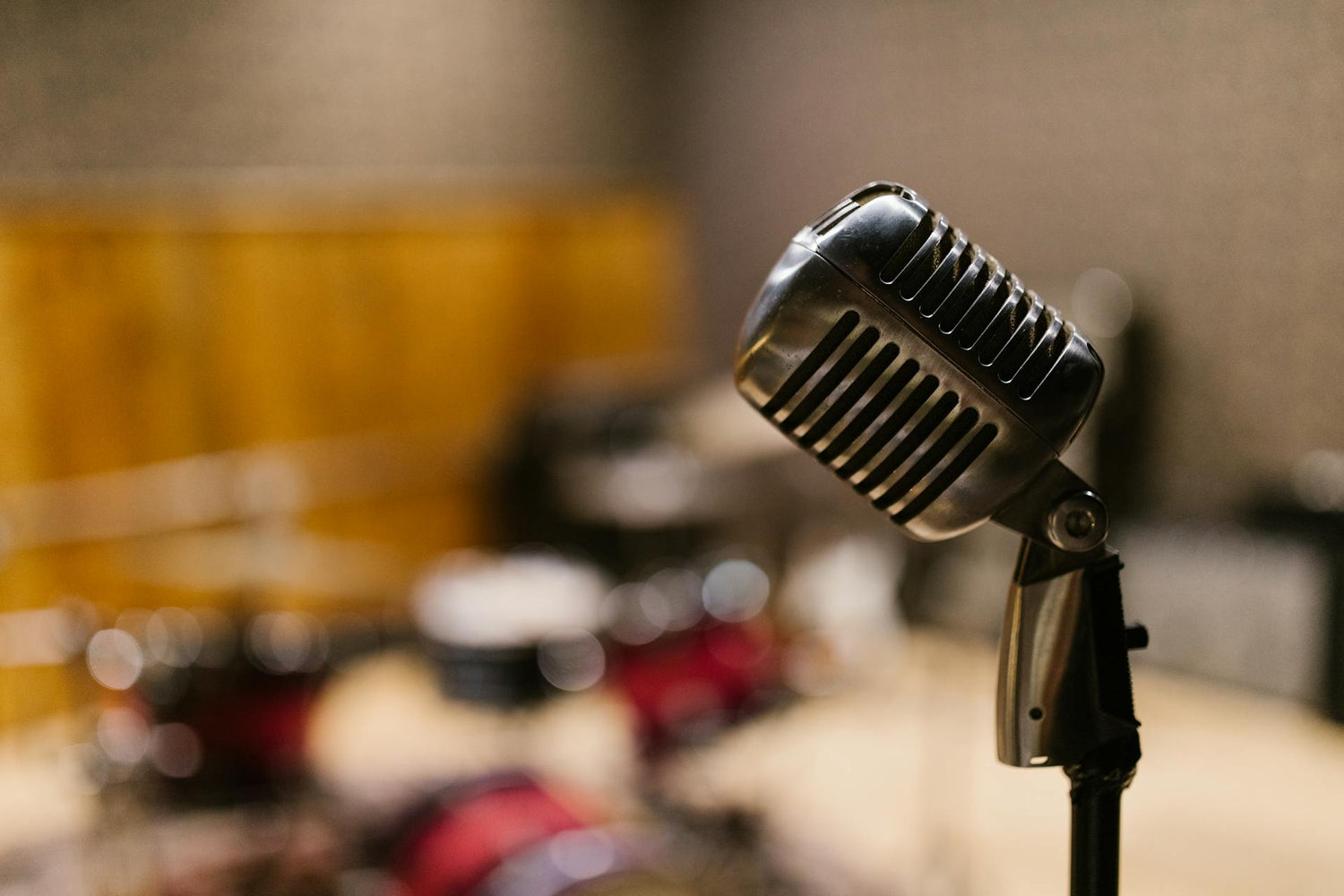 Vintage style microphone in a recording studio with blurred drums in the background.