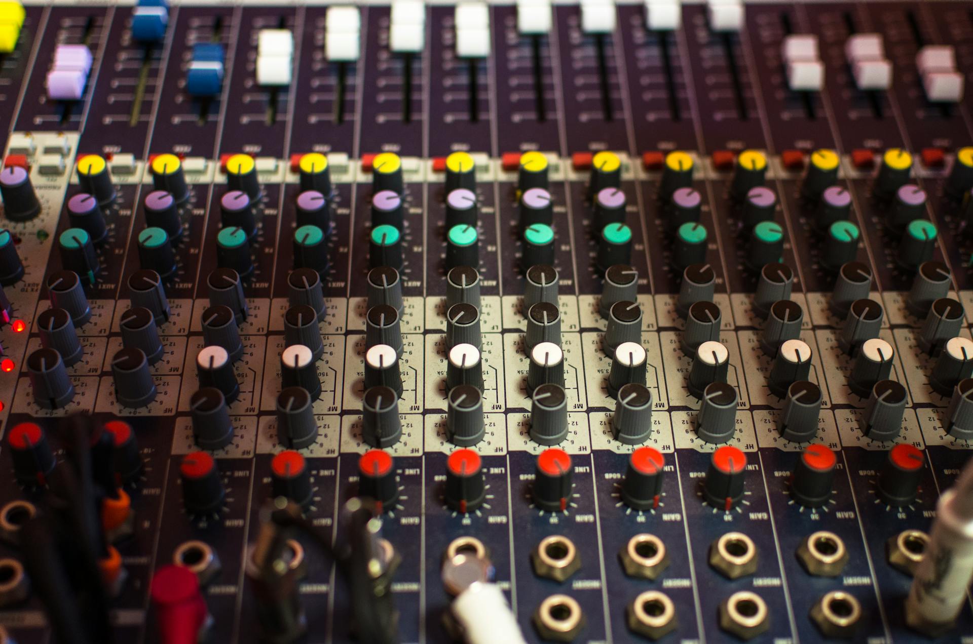 Close up of a colorful audio mixing console with knobs, sliders, and cables.