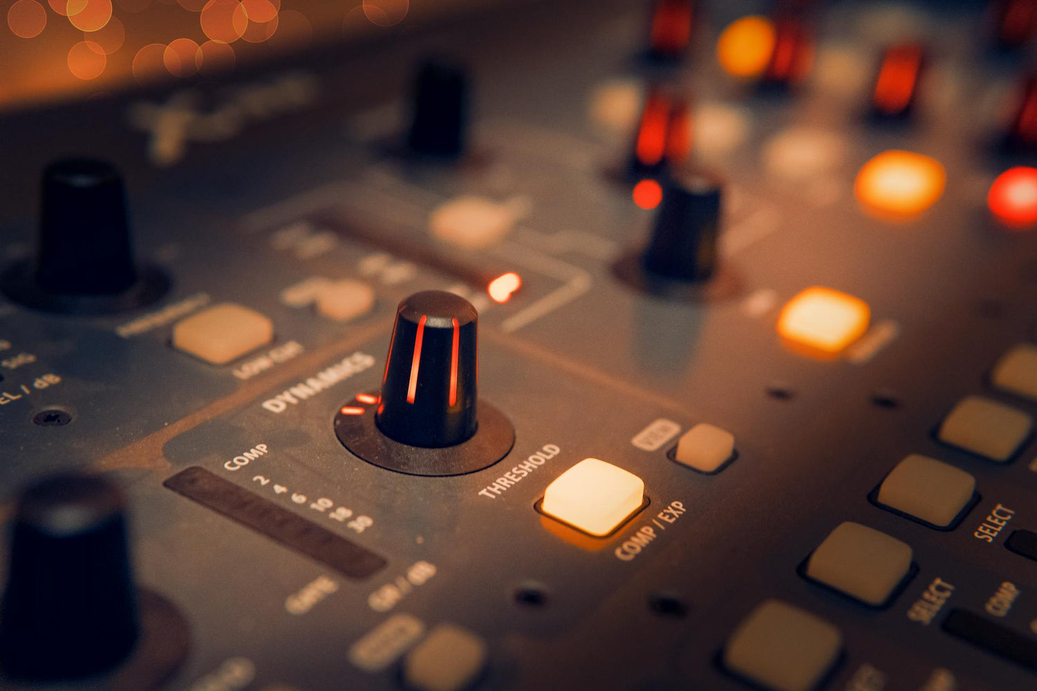 Close up of audio equipment control panel with glowing lights, buttons, and knobs in a studio environment.